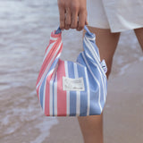 Person holding a striped bag with a blurred beach background