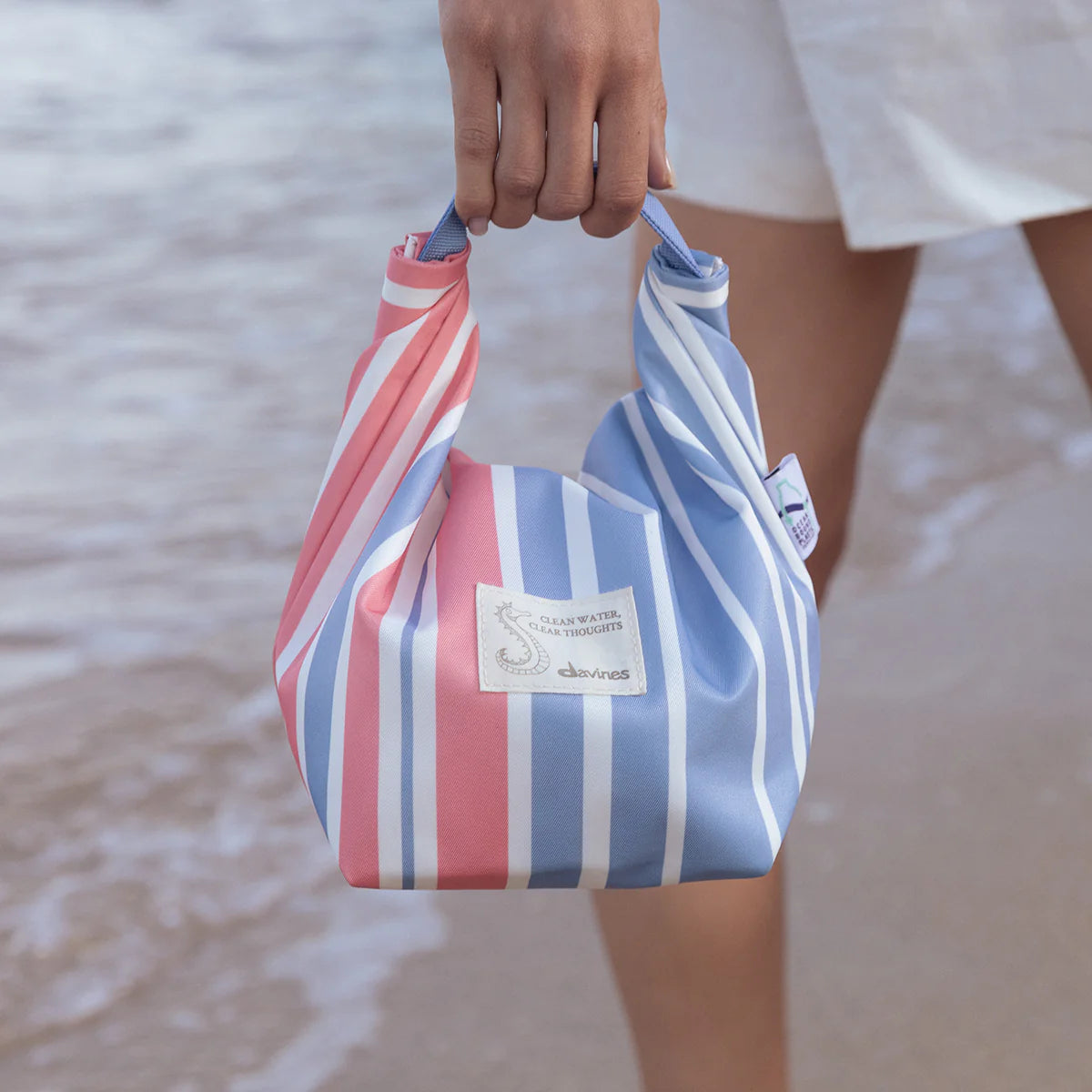Person holding a striped bag with a blurred beach background