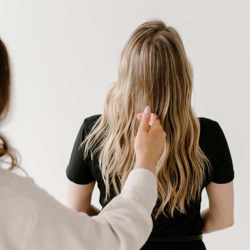 Person adjusting another person's hair against a plain background