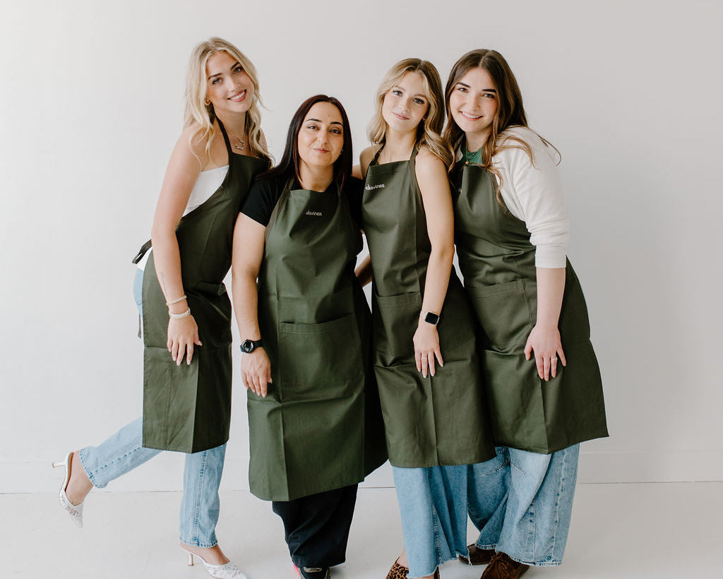 Four women wearing green aprons standing against a white background