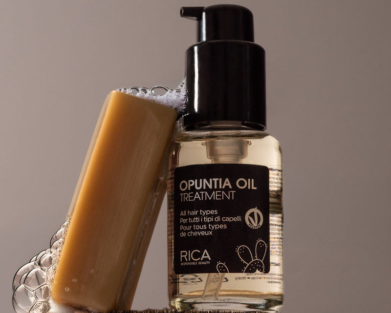 RICA Opuntia Oil Treatment bottle with a brush and bar of soap on a wooden block against a neutral background