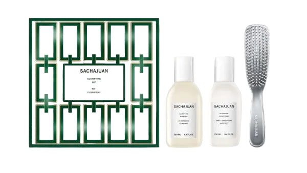 Sachajuan Clarifying Kit set featuring a green and white geometric-patterned box, two white bottles of shampoo and conditioner, and a silver hairbrush on a light gray background with reflections.