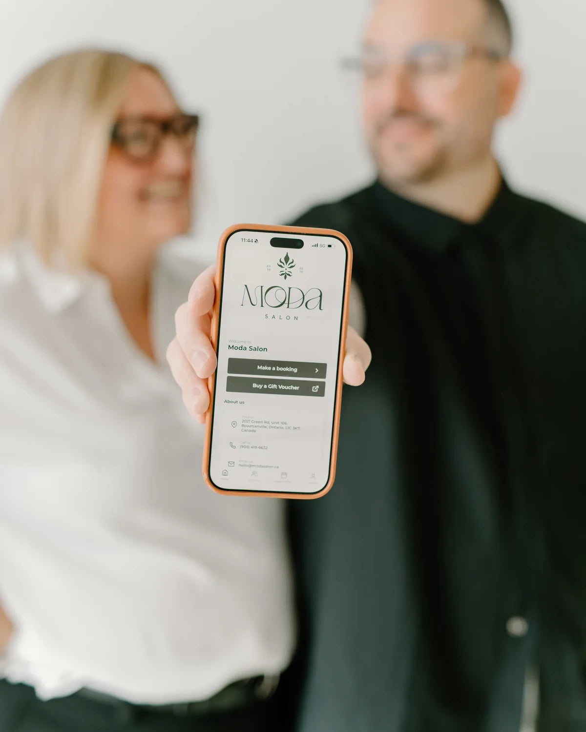 Kris and Chantelle holding a phone showing the Moda Salon booking app
